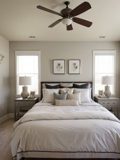 a bedroom with a bed, ceiling fan and two windows in the room above it