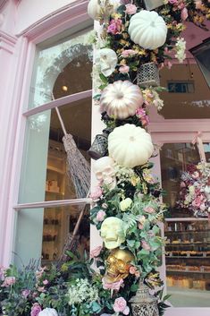 a tall display of flowers and pumpkins in front of a store window with pink trim