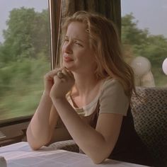 a woman sitting at a table in front of a window and looking out the window