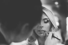 a woman getting her make - up done in front of a mirror while another person looks on