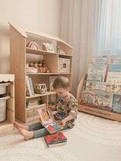 a young boy sitting on the floor reading a book in front of a wooden doll house