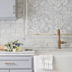 a white sink sitting under a window next to a counter top with flowers on it