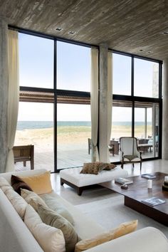 a living room filled with lots of furniture next to large glass windows overlooking the ocean