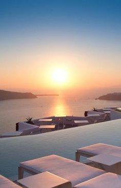 the sun is setting over an ocean with lounge chairs