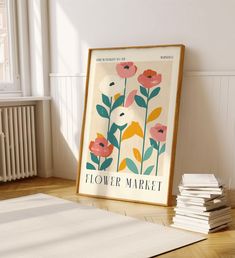 a framed flower market poster sitting on top of a hard wood floor next to a stack of books