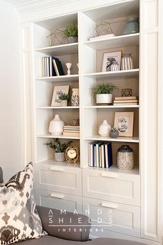 a white bookcase filled with lots of books next to a gray couch and pillows