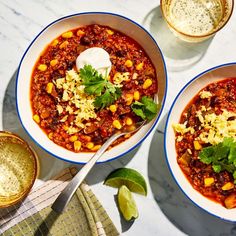 two bowls of chili with sour cream and cilantro garnish on the side