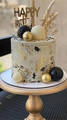 a white and gold birthday cake with black and gold decorations on it's side