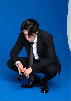 a man in a suit and tie sitting on the ground with his hands clasped to his knees