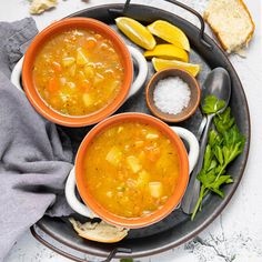 three bowls of soup on a plate with bread and lemon wedges next to it