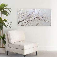 a white chair sitting next to a potted plant in front of a painting on the wall