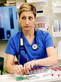 a woman in blue scrubs sitting at a table with medical supplies on top of it