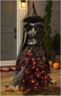 a lighted halloween tree with a witch hat and broom on it's head, in front of a door