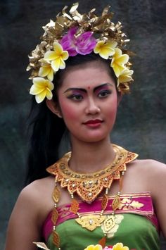 a woman with flowers in her hair wearing a green and pink dress holding a plate