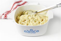 a white bowl filled with mashed potatoes on top of a table next to a red and white napkin