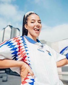 a woman with her hands on her hips wearing a white shirt and blue and red checkered sleeves