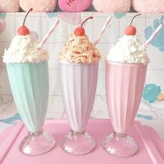 three milkshakes with whipped cream and cherries in them on a pink tray