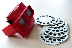 a red camera sitting on top of a table next to some white plates and discs