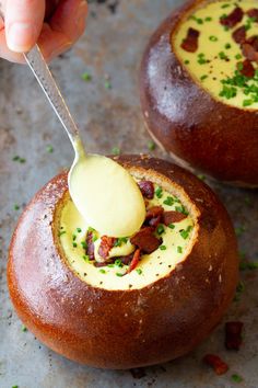 a person spooning something out of a bread bowl with bacon and cheese in it