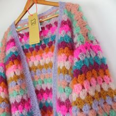 a multicolored crocheted sweater hanging on a wooden hanger with a price tag