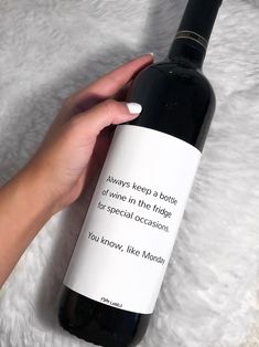 a woman's hand holding a bottle of wine on top of a white blanket