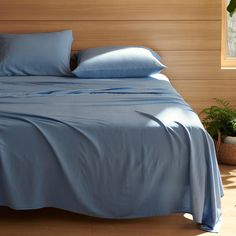 a bed with blue sheets and pillows in a room next to a plant on the floor