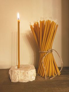 a bunch of yellow candles sitting on top of a wooden table next to a rock