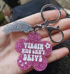 a person holding a pink flower shaped keychain that says virgin, who can't drive