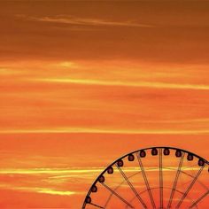 an orange sky with a ferris wheel in the foreground and a plane flying overhead