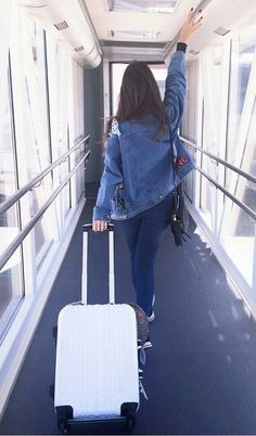 a woman is walking with her luggage down the hall way and waving to someone in the distance