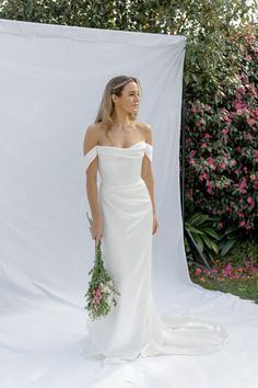 a woman in a white wedding dress holding a flower bouquet and posing for a photo