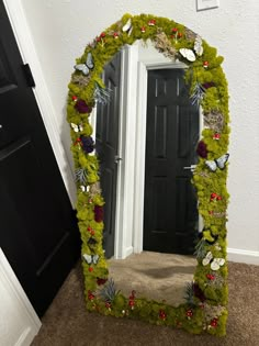 a mirror that is sitting on the ground in front of a door with flowers and grass