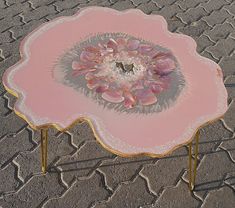 a pink and gold coffee table with flowers on it's center piece, in the middle of a cobblestone area