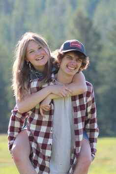 a boy and girl hug each other while standing in front of a field with trees