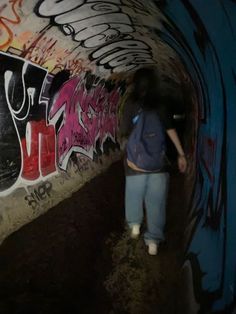 a man walking through a tunnel covered in graffiti