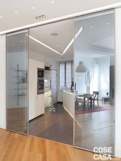 an open glass door leading to a kitchen and dining room with wood flooring in front of it