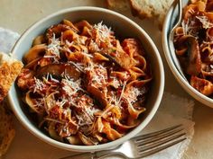 two bowls of pasta with mushrooms and parmesan cheese on the side next to bread