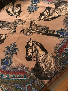 a table cloth with horses and flowers on it, sitting on top of a wooden table