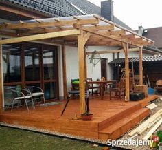 a wooden deck in front of a house with an attached pergolan over it