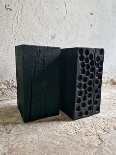 two black speakers sitting next to each other on top of a cement floor covered ground