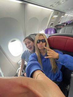 two women on an airplane pointing at the camera