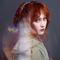 a woman with red hair wearing a white dress and pearls on her head is looking at the camera