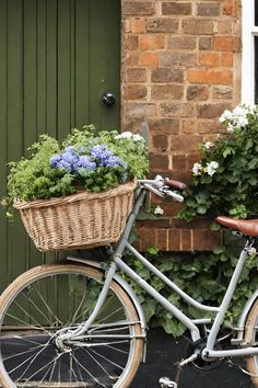 a bicycle with flowers in the basket is parked next to a brick wall and green door