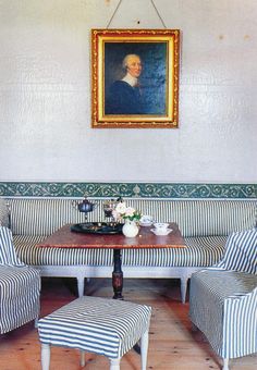 a painting hangs on the wall above a striped bench and ottoman in a dining room