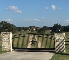 an iron gate with a star on it in the middle of a grassy area next to a driveway