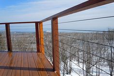 a wooden deck with railings and snow on the ground in front of some trees