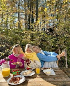 two women sitting at a picnic table with food and orange juices on the side