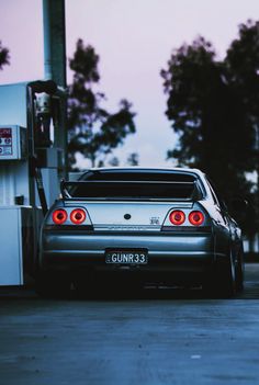 the back end of a car parked in front of a gas station with trees behind it