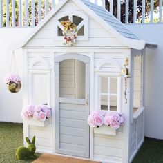 a small white doll house sitting on top of a grass covered field next to a pink chair