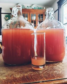 two glass jugs filled with liquid sitting on top of a wooden table